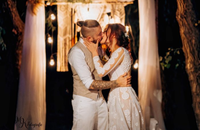 Ein Paar küsst sich romantisch vor einer festlich dekorierten Kulisse mit Lichtern.